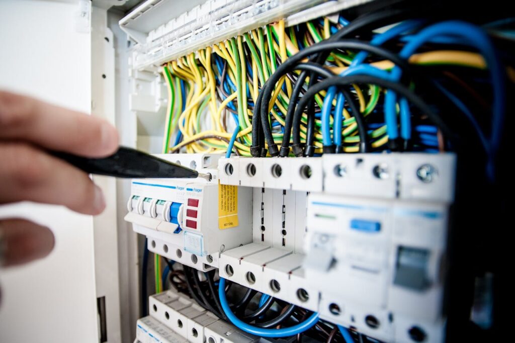 pexels-photo-257736-1 Hand of electrician working on a circuit breaker panel with colorful wires, ensuring safe electrical connections.